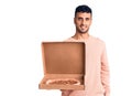 Young hispanic man holding delivery pizza box looking positive and happy standing and smiling with a confident smile showing teeth Royalty Free Stock Photo