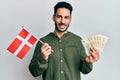 Young hispanic man holding denmark flag and krone banknotes smiling with a happy and cool smile on face Royalty Free Stock Photo