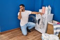 Young hispanic man holding dirty clothe closing nose at laundry room Royalty Free Stock Photo