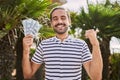 Young hispanic man holding dollars close to face pointing thumb up to the side smiling happy with open mouth Royalty Free Stock Photo