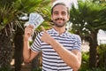 Young hispanic man holding dollars close to face smiling happy pointing with hand and finger Royalty Free Stock Photo