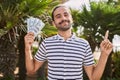 Young hispanic man holding dollars close to face smiling happy pointing with hand and finger to the side Royalty Free Stock Photo