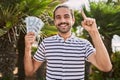 Young hispanic man holding dollars close to face smiling with an idea or question pointing finger with happy face, number one Royalty Free Stock Photo