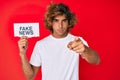 Young hispanic man holding fake news banner pointing with finger to the camera and to you, confident gesture looking serious Royalty Free Stock Photo