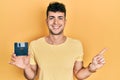 Young hispanic man holding floppy disk smiling happy pointing with hand and finger to the side Royalty Free Stock Photo