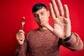 Young hispanic man holding fresh organic tomato on fork over red isolated background with open hand doing stop sign with serious Royalty Free Stock Photo