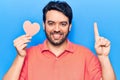 Young hispanic man holding heart shape paper smiling with an idea or question pointing finger with happy face, number one Royalty Free Stock Photo