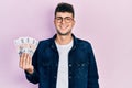 Young hispanic man holding icelandic krona banknotes looking positive and happy standing and smiling with a confident smile