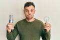 Young hispanic man holding lightbulb for inspiration and idea puffing cheeks with funny face
