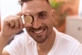 Young hispanic man holding litecoin crypto currency over eye at home