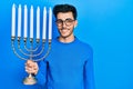 Young hispanic man holding menorah hanukkah jewish candle looking positive and happy standing and smiling with a confident smile Royalty Free Stock Photo