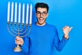 Young hispanic man holding menorah hanukkah jewish candle pointing thumb up to the side smiling happy with open mouth Royalty Free Stock Photo