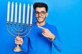 Young hispanic man holding menorah hanukkah jewish candle smiling happy pointing with hand and finger Royalty Free Stock Photo