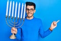 Young hispanic man holding menorah hanukkah jewish candle smiling happy pointing with hand and finger to the side Royalty Free Stock Photo