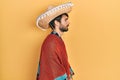 Young hispanic man holding mexican hat looking to side, relax profile pose with natural face with confident smile