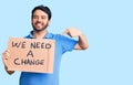 Young hispanic man holding we need a change banner pointing finger to one self smiling happy and proud