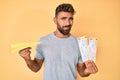 Young hispanic man holding paper airplane and boarding pass clueless and confused expression Royalty Free Stock Photo