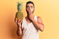 Young hispanic man holding pineapple covering mouth with hand, shocked and afraid for mistake Royalty Free Stock Photo