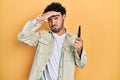 Young hispanic man holding pocket knife stressed and frustrated with hand on head, surprised and angry face Royalty Free Stock Photo