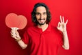 Young hispanic man holding red ping pong rackets doing ok sign with fingers, smiling friendly gesturing excellent symbol