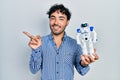 Young hispanic man holding robot toy smiling happy pointing with hand and finger to the side