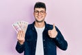 Young hispanic man holding saudi arabia riyal banknotes smiling happy and positive, thumb up doing excellent and approval sign Royalty Free Stock Photo