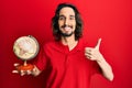 Young hispanic man holding small world ball smiling happy and positive, thumb up doing excellent and approval sign Royalty Free Stock Photo