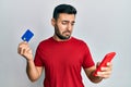 Young hispanic man holding smartphone and credit card depressed and worry for distress, crying angry and afraid Royalty Free Stock Photo