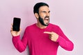 Young hispanic man holding smartphone showing blank screen angry and mad screaming frustrated and furious, shouting with anger Royalty Free Stock Photo