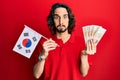 Young hispanic man holding south korea flag and won banknotes puffing cheeks with funny face Royalty Free Stock Photo