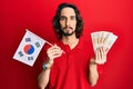 Young hispanic man holding south korea flag and won banknotes relaxed with serious expression on face Royalty Free Stock Photo