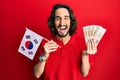 Young hispanic man holding south korea flag and won banknotes smiling and laughing hard out loud because funny crazy joke Royalty Free Stock Photo