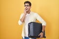 Young hispanic man holding suitcase going on summer vacation bored yawning tired covering mouth with hand Royalty Free Stock Photo