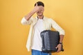 Young hispanic man holding suitcase going on summer vacation covering eyes with hand, looking serious and sad Royalty Free Stock Photo