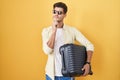 Young hispanic man holding suitcase going on summer vacation with hand on chin thinking about question, pensive expression Royalty Free Stock Photo