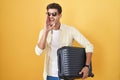 Young hispanic man holding suitcase going on summer vacation hand on mouth telling secret rumor, whispering malicious talk Royalty Free Stock Photo