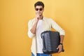 Young hispanic man holding suitcase going on summer vacation thinking worried about a question, concerned and nervous with hand on Royalty Free Stock Photo