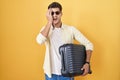 Young hispanic man holding suitcase going on summer vacation yawning tired covering half face, eye and mouth with hand Royalty Free Stock Photo