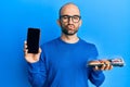 Young hispanic man holding take away food showing smartphone screen looking at the camera blowing a kiss being lovely and sexy