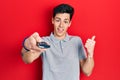 Young hispanic man holding television remote control pointing thumb up to the side smiling happy with open mouth Royalty Free Stock Photo