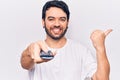 Young hispanic man holding television remote control pointing thumb up to the side smiling happy with open mouth Royalty Free Stock Photo