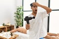 Young hispanic man holding therapy massage gun at wellness center stressed and frustrated with hand on head, surprised and angry Royalty Free Stock Photo