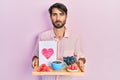 Young hispanic man holding tray with breakfast food and heart draw relaxed with serious expression on face Royalty Free Stock Photo