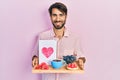 Young hispanic man holding tray with breakfast food and heart draw smiling with a happy and cool smile on face Royalty Free Stock Photo