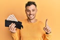 Young hispanic man holding wallet with united kingdom pounds smiling with an idea or question pointing finger with happy face,