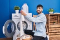 Young hispanic man holding white t shirt washing clothes at laundry room