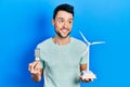 Young hispanic man holding windmill and led lightbulb smiling looking to the side and staring away thinking Royalty Free Stock Photo