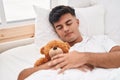 Young hispanic man hugging teddy bear lying on bed sleeping at bedroom Royalty Free Stock Photo