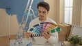 Young hispanic man indoors selecting paint colors with samples in a home interior setting featuring ladders and unpacked boxes Royalty Free Stock Photo