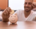 Young hispanic man inserting litecoin crypto currency on piggy bank at home